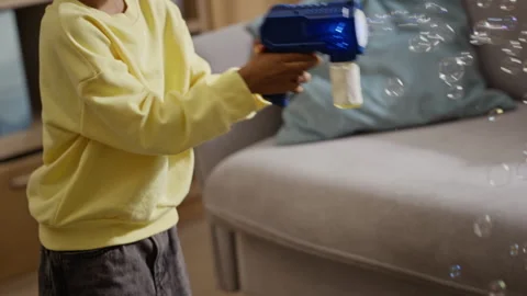 Happy Black Boy Playing with Automatic Toy Bubble Gun at Home Stock Footage 345491578