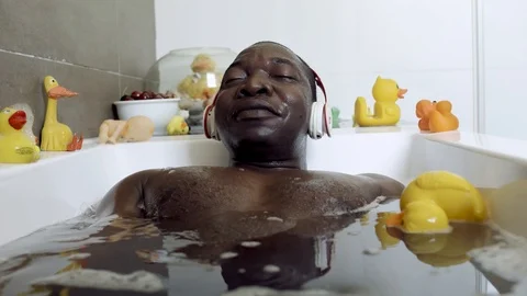 Happy Black man playing with rubber ducks and hearing music while taking a bath. Stock Footage 112019337