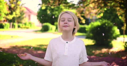 Happy blond boy under the rain of blossoms in spring garden at sunny day Stock Footage 170432885