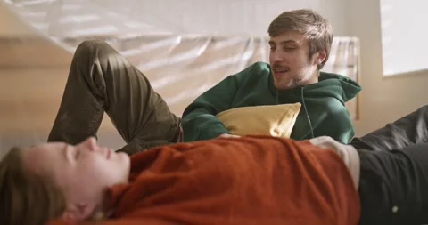 A happy blond guy in a green jacket is talking with his girlfriend who is lying Video stock 309468656