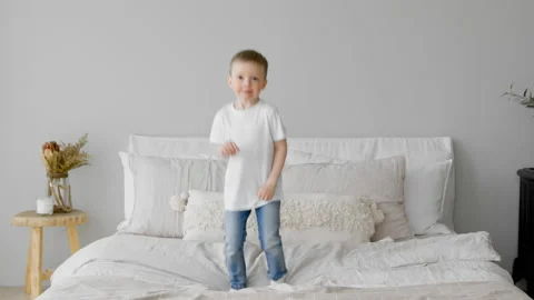 Happy blonde 4-year-old child is having fun jumping on bed, rejoicing and Stock Footage