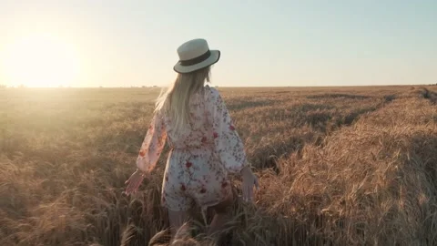 Happy blonde in a dress and hat runs on a field of wheat. Stock Footage