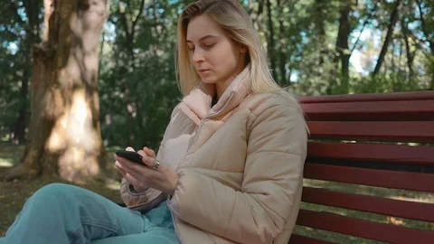Happy blonde girl student using a smartphone in a city park, young woman use Stock Footage 117410237