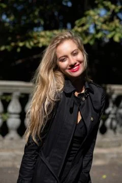 Happy blonde model wearing black coat and dress posing in rays of sun at the  Stock Photos