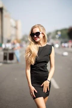 Happy blonde model wearing black dress and sunglasses, walking down the sunny Stock Photos