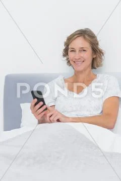 Happy blonde woman sending text message in bed Stock Photos