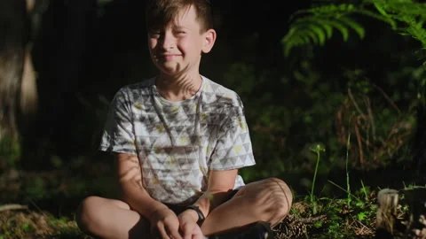 Happy boy 9 years old looking at camera sitting in forest in nature Stock Footage 135334150