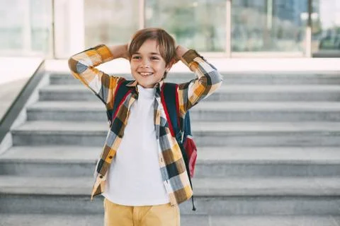A happy boy with a backpack stands on the steps in front of the entrance to t Stock Photos