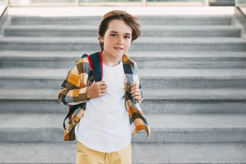 A happy boy with a backpack stands on the steps in front of the entrance to t Stock Photos