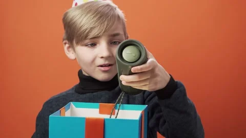 Happy boy in birthday hat opens a gift box on orange background. Stock Footage 164397291