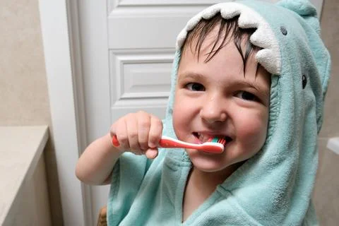 Happy boy brushing his teeth with a child toothbrush in a shark hood towel. O Stock Photos