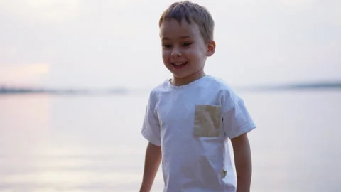Happy boy clapping hands by the lake at sunset. Close portrait of smiling child Stock Footage 336383353