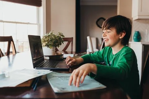 Happy boy doing on school work online on computer at kitchen table. 스톡 사진