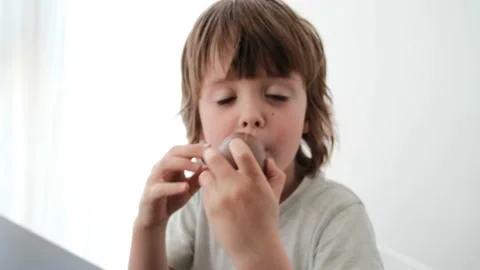 Happy boy eats chocolate egg with surprise near white wall Stock Footage 154390643