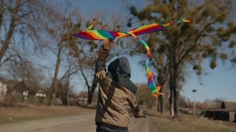 A happy boy with a flying rainbow kite rides a bicycle on the road. Stockbeeldmateriaal 191972632