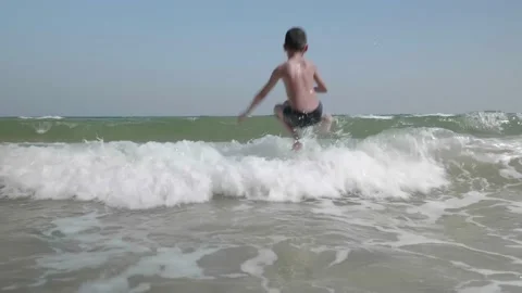 A happy boy has fun to sits and jumping over the waves onto the beach. Stock Footage 146692563