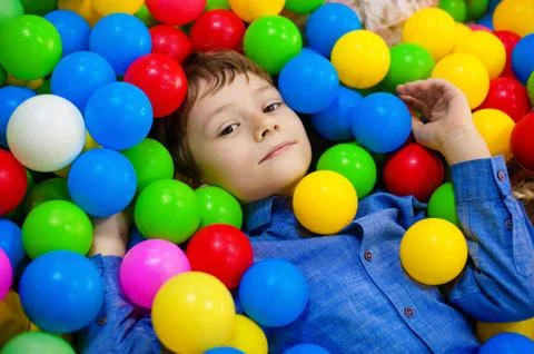 Happy boy having fun in ball pit on birthday party in kids amusement park and Stock Photos