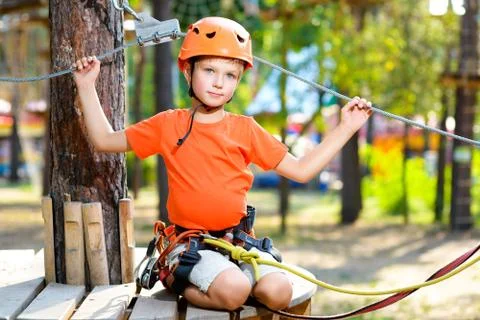 Happy boy having fun when playing at adventure park, holding ropes and sitting Stock Photos