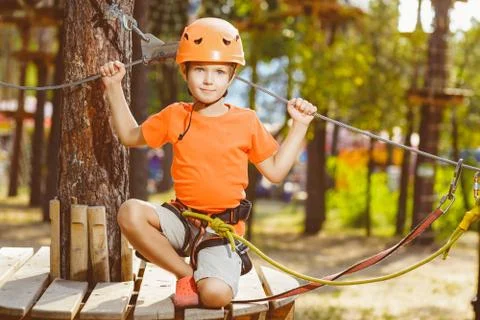 Happy boy having fun when playing at adventure park, holding ropes and sitting Stock Photos