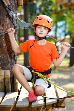 Happy boy having fun when playing at adventure park, holding ropes and sitting Stock Photos