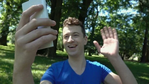 Happy boy having a videocall on smartphone in the park, slow motion shot at 240f Stock Footage 77002575