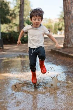 Happy boy jumping in mud puddle with boots 스톡 사진
