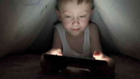 A happy boy lies in bed under a blanket and plays on mobile phone in a game in Stock Footage 147388925