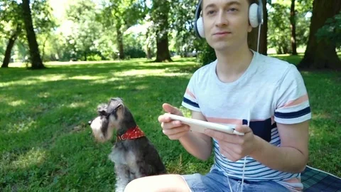 Happy boy listening music while relaxing in the park with his dog, steadycam sho Stock-Footage 77002016