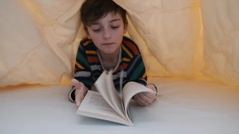 A happy boy is lying in bed under a yellow blanket and reading a book Stock Footage 105268517