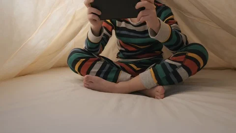 A happy boy is lying in bed under a yellow blanket playing the game tablet Stock Footage 105268723