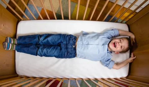 Happy boy lying in a cot with arms and legs stretched Stock Photos