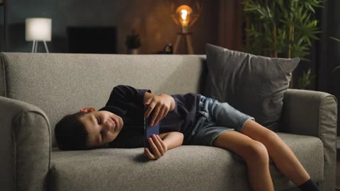 Happy Boy Lying on Sofa Laughing while Using Smartphone 스톡 동영상 344146428