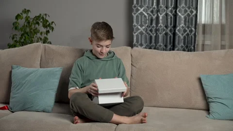 Happy boy opens a gift sitting on the sofa in the living room. Child pulling the Stock Footage 265781524