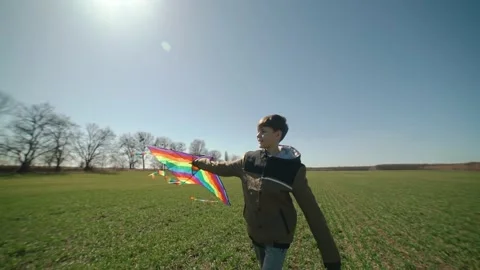 A happy boy is playing with a flying rainbow kite. Spinning in a green field. Stock Footage 192336714
