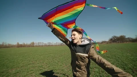 A happy boy is playing with a flying rainbow kite. Stock Footage 192336905