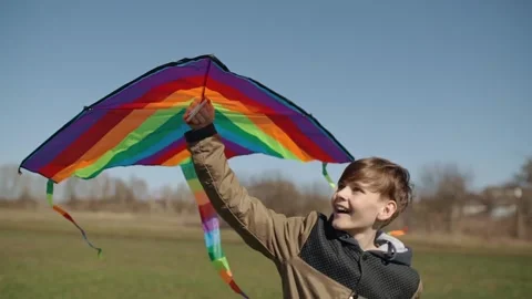 A happy boy is playing with a flying rainbow kite. Видео 192943594