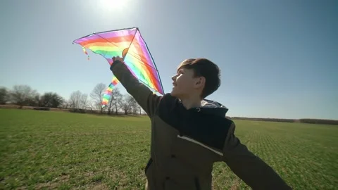 A happy boy is playing with a flying rainbow kite. Видео 194453107