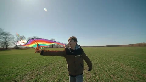 A happy boy is playing with a flying rainbow kite. Видео 194453171