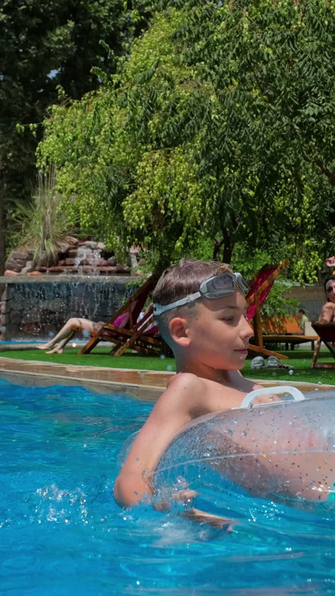 Happy boy playing in a pool on a sunny summer day, splashing water relaxing in Stock Footage 313227483