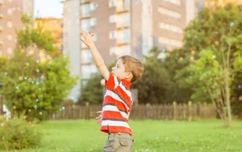Happy boy playing with soap bubbles in the park Stock Photos