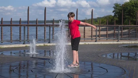 Happy boy playing with splash pad water fountain, sunny summer day, slow motion 库存影片 341519227