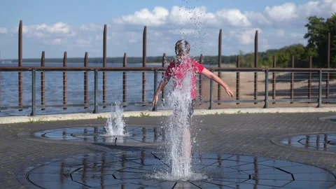 Happy boy playing with splash pad water fountain, sunny summer day, slow motion 库存影片 341519229