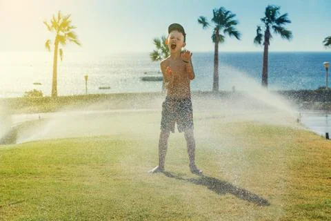 Happy boy playing with sprinklers near sea Stock Photos