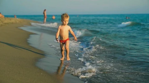 Happy boy run and jump merrily and splashing in the sea water in sunset. Slowmo Stock Footage 107831176