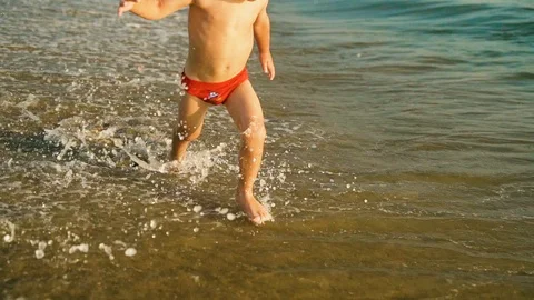 Happy boy run and jump merrily and splashing in the sea water in sunset. Slowmo Stock Footage 107832011