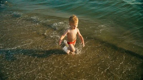 Happy boy run and jump merrily and splashing in the sea water in sunset. Slowmo Stock Footage 107832482