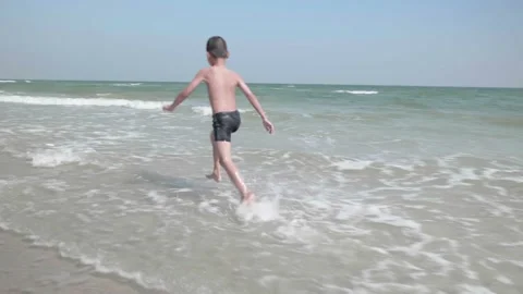 A happy boy runs on the beach with the waves crashing on the shore. Stock Footage 146692523