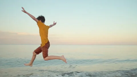 Happy boy runs in clothes jumping into sea, waving his arms, smiles Stock Footage 135028672