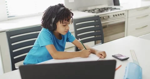 Happy boy sitting at table in kitchen using laptop and doing homework Stock Footage 335364259