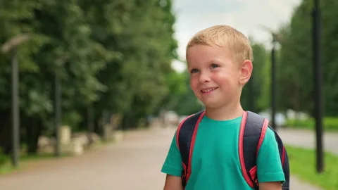 Happy boy smiling and wearing a school backpack standing in a park. Cute sm.. Video stock 339534302